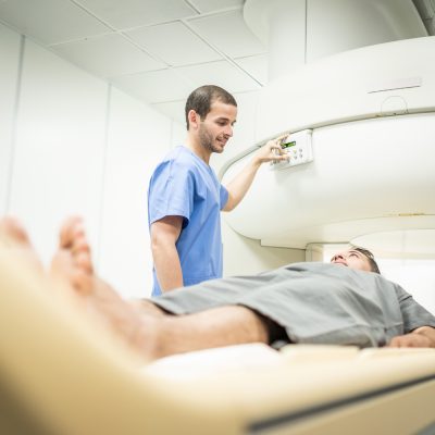 Middle aged patient with cancer and nurse during MRI in hospital lab. Man ins his 40s with doctor in clinic during medical examination. People and disease prevention with magnetic resonance imaging. Front side